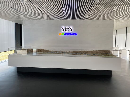 Ein modernes Ausstellungsmodell mit dem beleuchteten Logo von SES steht in einem stilvollen, hellen Raum.