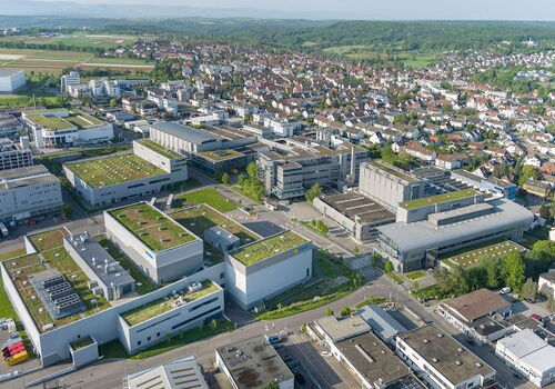 Luftaufnahme des Herma Betriebsgeländes mit begrünten Dächern, umgeben von einer weitläufigen Stadtlandschaft.