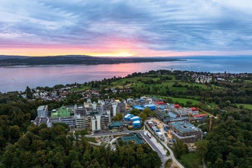 Luftaufnahme eines Campus am Bodensee bei Sonnenuntergang, umgeben von grünen Wiesen und bewaldeten Hügeln.