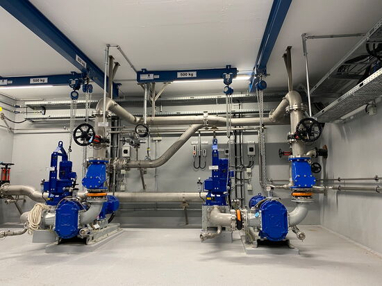 Ein moderner Technikraum zeigt blaue Maschinen und silberne Rohrleitungen, die präzise für industrielle Anwendungen positioniert sind.