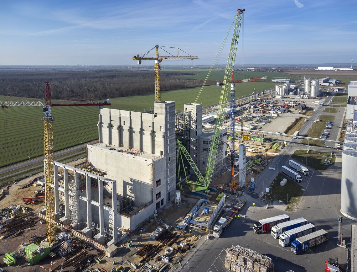 Eine große Baustelle in Sandersdorf zeigt Kräne und Baufortschritte neben grünen Feldern unter klarem Himmel.