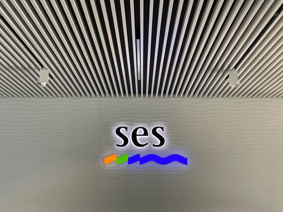 Ein modernes Büro mit wellenförmiger Wand zeigt das beleuchtete Logo "ses" unter einer strukturierten Deckenverkleidung.