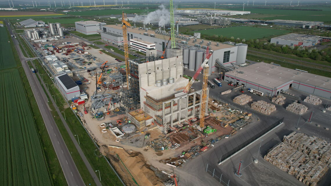 Eine Drohnenaufnahme zeigt eine große Baustelle mit Kränen und Gebäuden in einem Industriegebiet.