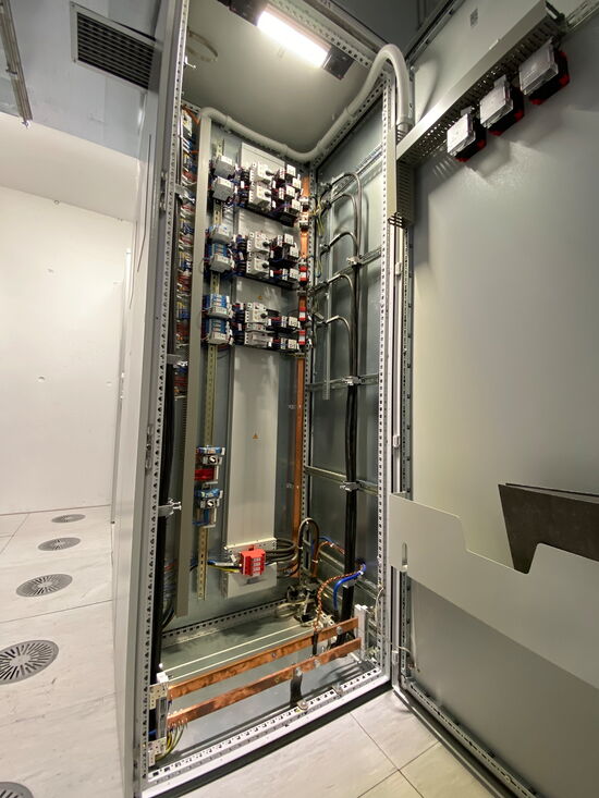 Ein geöffneter Schaltschrank zeigt komplexe Verkabelung und Elektronik in einem hell erleuchteten Technikraum.
