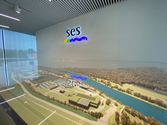 Ein detailliertes Architekturmodell zeigt eine Anlage mit Gebäuden und Flusslandschaft unter dem Logo von SES.