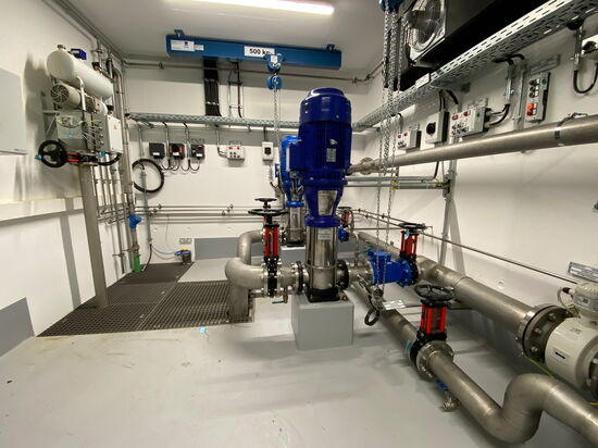Ein moderner Maschinenraum zeigt Rohrleitungen und einen blauen Motor, der von einem Kran mit 500 kg Kapazität unterstützt wird.