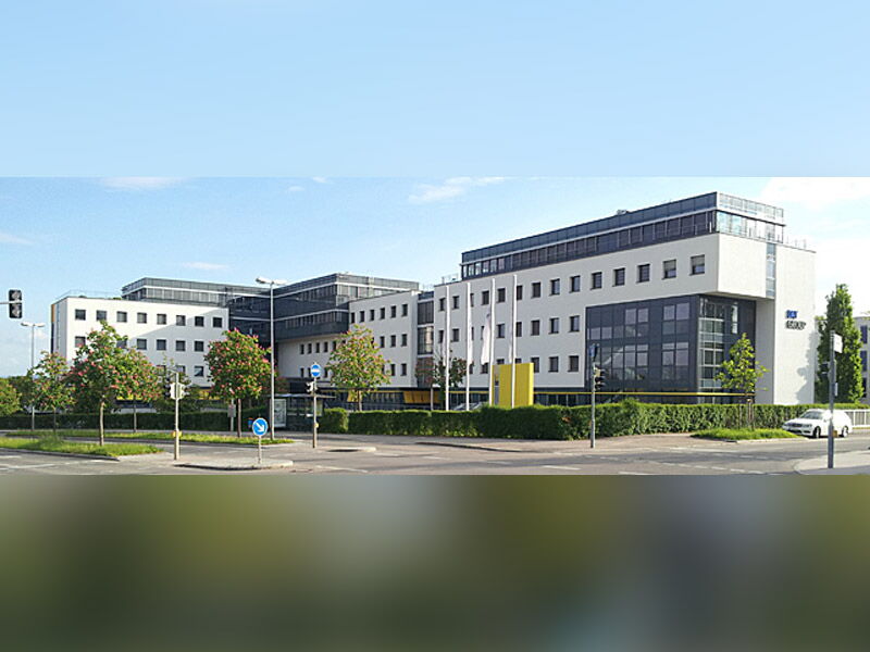 Ein modernes Bürogebäude mit großen Fenstern steht an einer Straßenecke unter klarem Himmel.